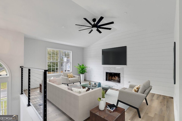 living room with lofted ceiling, ceiling fan, wood walls, a premium fireplace, and light hardwood / wood-style flooring