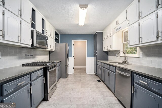 kitchen featuring decorative backsplash, a textured ceiling, stainless steel appliances, sink, and white cabinetry