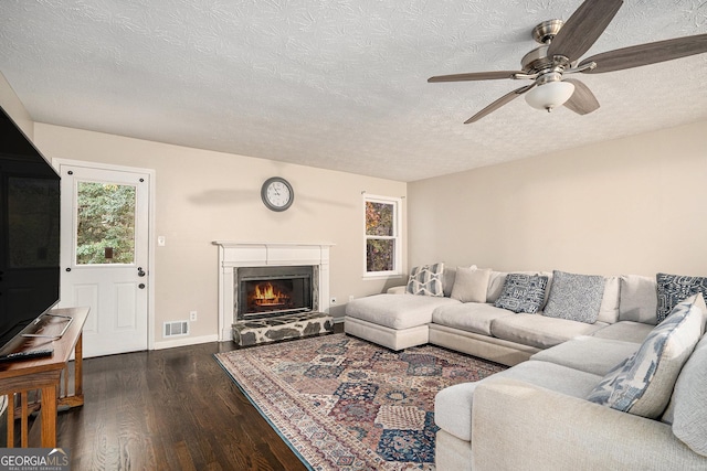 living room featuring a textured ceiling, a stone fireplace, ceiling fan, and dark hardwood / wood-style floors