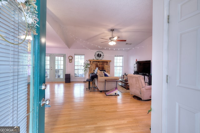 living room featuring ceiling fan, vaulted ceiling, a textured ceiling, a fireplace, and light wood-type flooring