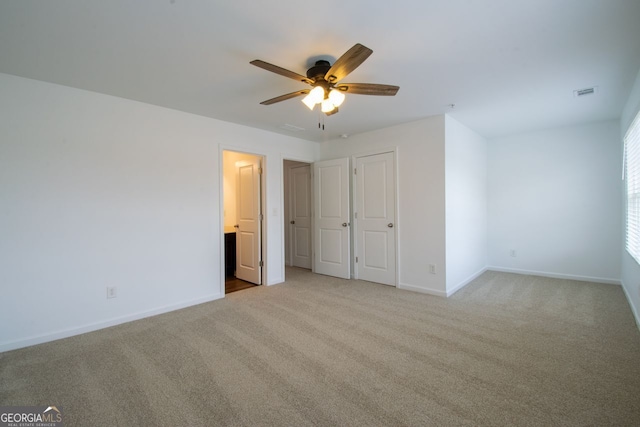 unfurnished bedroom featuring ceiling fan, ensuite bathroom, and light colored carpet