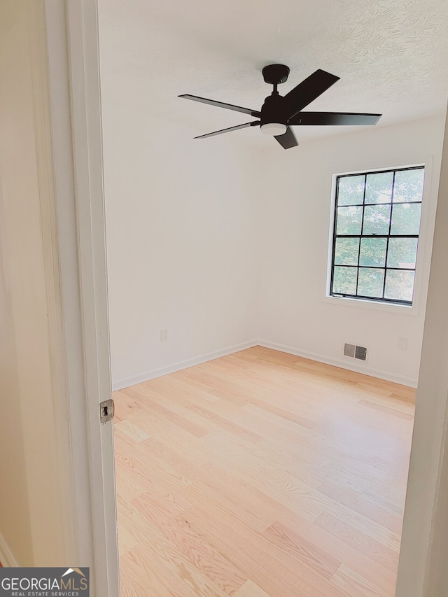 empty room with ceiling fan, a textured ceiling, and light wood-type flooring