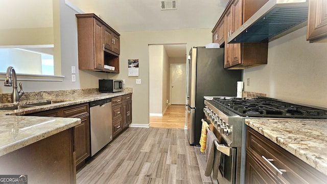 kitchen featuring light hardwood / wood-style flooring, sink, wall chimney range hood, stainless steel appliances, and light stone counters