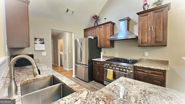 kitchen with sink, wall chimney exhaust hood, light hardwood / wood-style floors, lofted ceiling, and appliances with stainless steel finishes