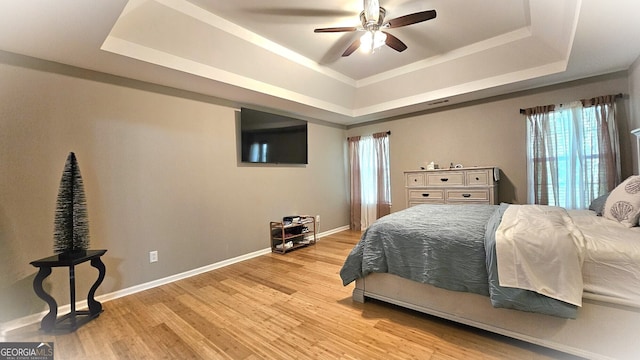 bedroom featuring ceiling fan, a raised ceiling, and light wood-type flooring