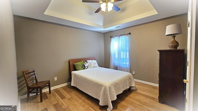 bedroom with a tray ceiling, ceiling fan, and light hardwood / wood-style flooring