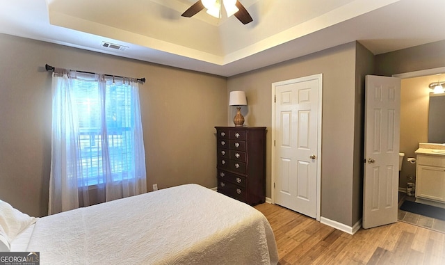 bedroom featuring a raised ceiling, connected bathroom, light hardwood / wood-style flooring, and ceiling fan