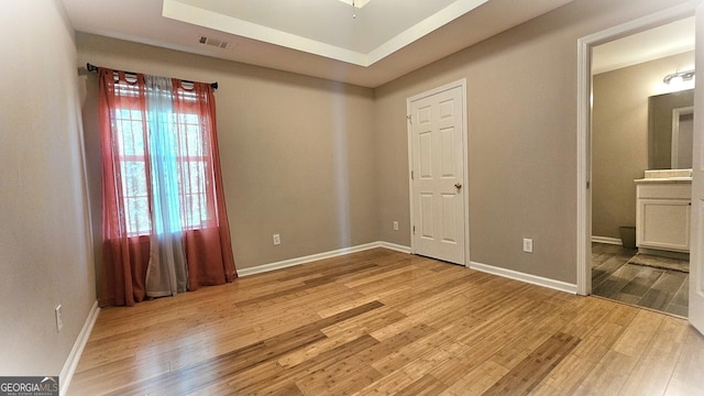 unfurnished bedroom featuring light hardwood / wood-style floors, a tray ceiling, and ensuite bathroom