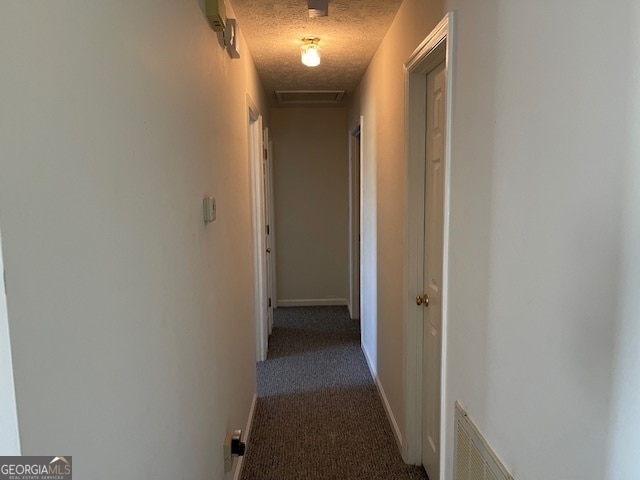 hallway featuring a textured ceiling and dark colored carpet