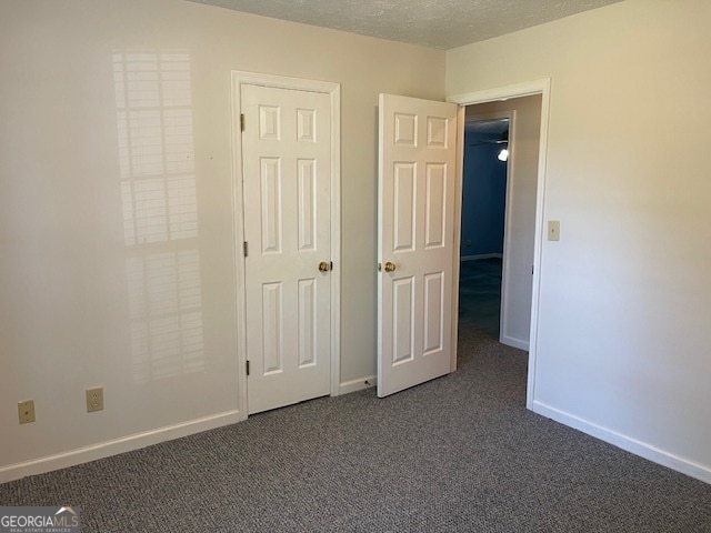 unfurnished bedroom featuring a textured ceiling and dark carpet