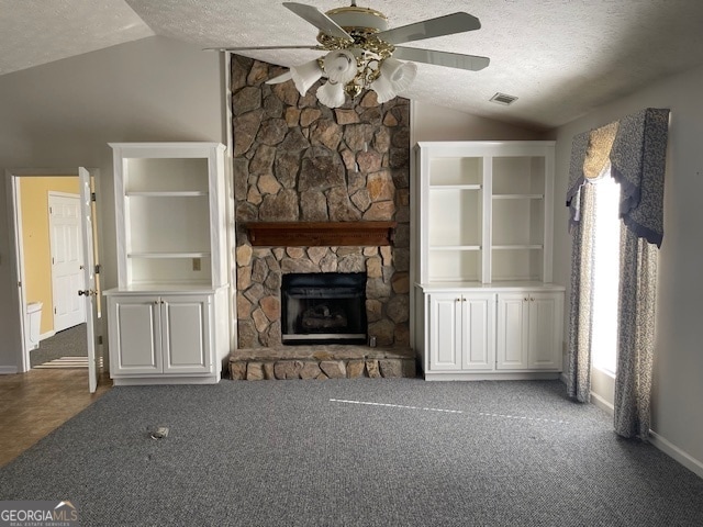 unfurnished living room with ceiling fan, a textured ceiling, a stone fireplace, lofted ceiling, and carpet floors