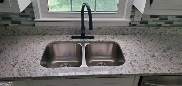 room details with white cabinetry, sink, tasteful backsplash, and light stone countertops