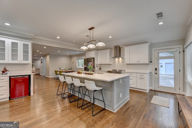 kitchen with white cabinets, wall chimney exhaust hood, light hardwood / wood-style floors, and decorative light fixtures