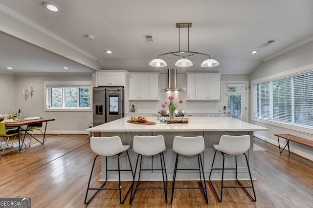 kitchen featuring light hardwood / wood-style floors, wall chimney exhaust hood, a large island, white cabinetry, and stainless steel fridge