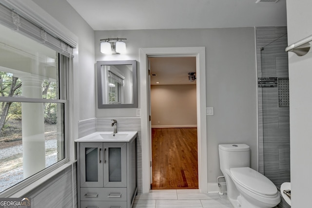 bathroom featuring hardwood / wood-style floors, vanity, toilet, and tiled shower