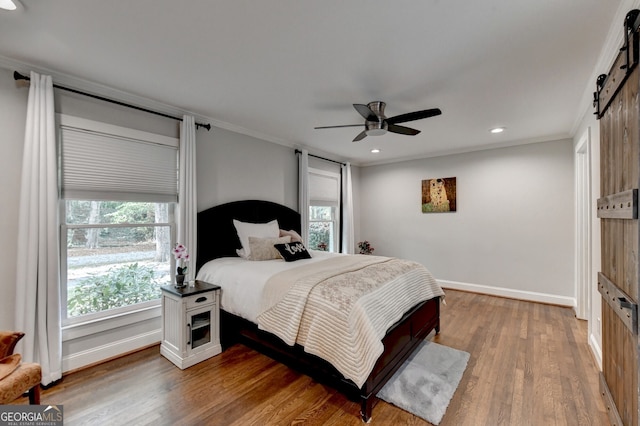 bedroom with a barn door, ceiling fan, multiple windows, and hardwood / wood-style floors