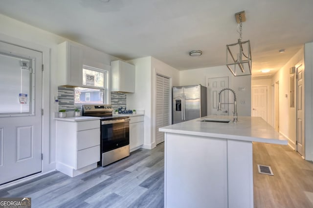 kitchen featuring appliances with stainless steel finishes, sink, white cabinets, hanging light fixtures, and an island with sink