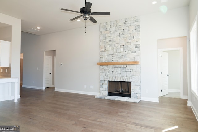 unfurnished living room with ceiling fan, a stone fireplace, and light hardwood / wood-style flooring