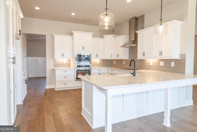 kitchen featuring wall chimney exhaust hood, white cabinetry, decorative light fixtures, appliances with stainless steel finishes, and kitchen peninsula