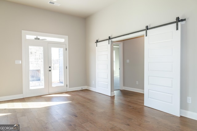 interior space with dark hardwood / wood-style floors, a barn door, ceiling fan, and french doors