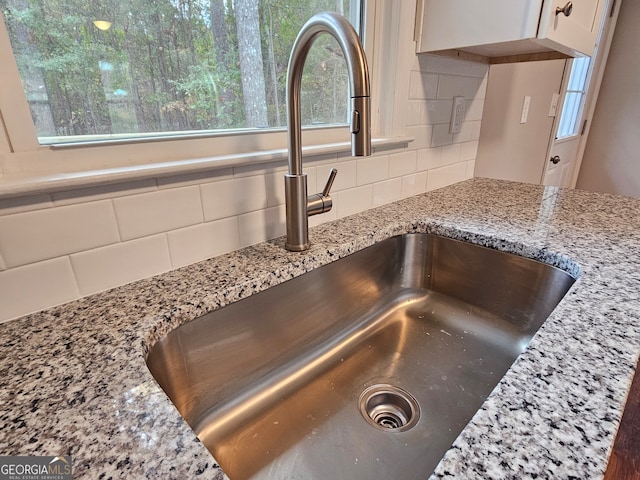 details featuring decorative backsplash, white cabinetry, sink, and light stone counters