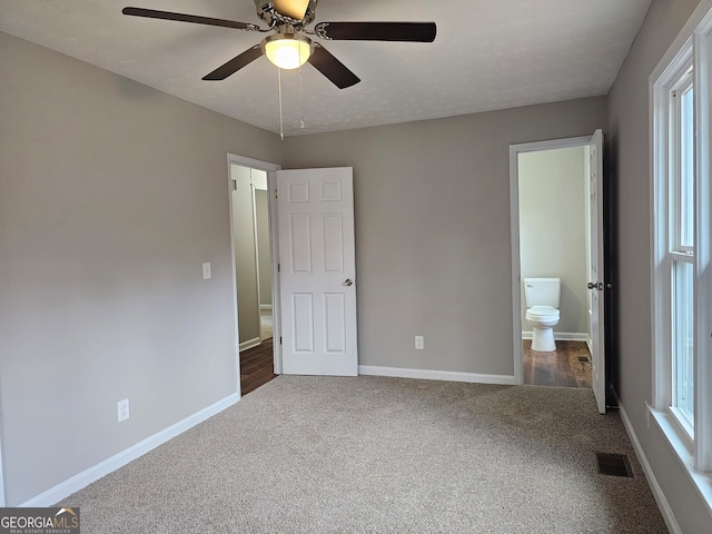 unfurnished bedroom with a textured ceiling, dark colored carpet, ceiling fan, and ensuite bathroom