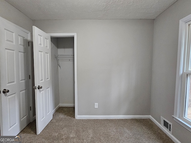 unfurnished bedroom featuring carpet floors, a textured ceiling, and a closet