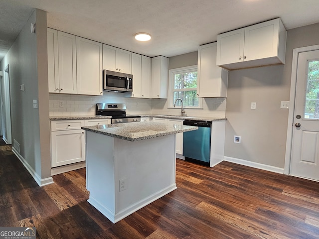 kitchen with white cabinets, dark hardwood / wood-style flooring, a kitchen island, and appliances with stainless steel finishes