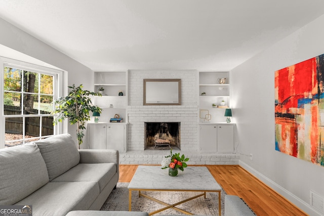 living room with built in shelves, a fireplace, and wood-type flooring