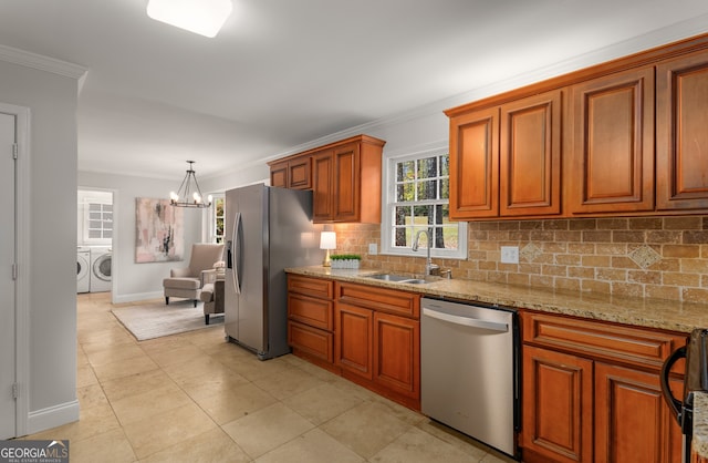 kitchen with pendant lighting, sink, ornamental molding, appliances with stainless steel finishes, and washing machine and clothes dryer