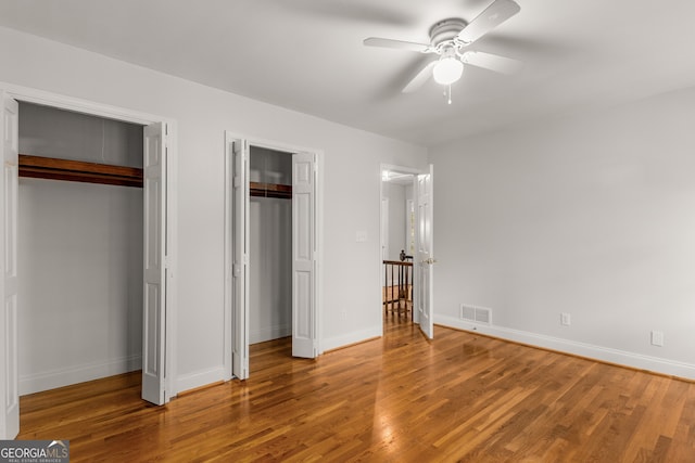 unfurnished bedroom featuring ceiling fan, wood-type flooring, and multiple closets