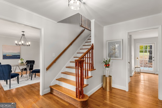 stairway featuring wood-type flooring, crown molding, and a chandelier