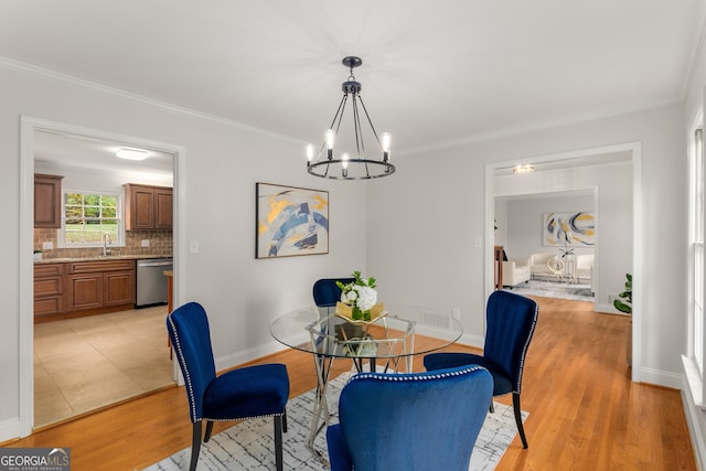 dining space with light wood-type flooring, an inviting chandelier, crown molding, and sink