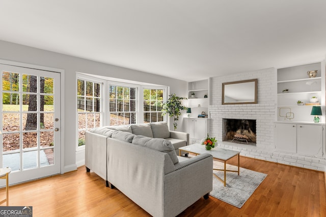 living room featuring a fireplace, built in shelves, light hardwood / wood-style flooring, and plenty of natural light