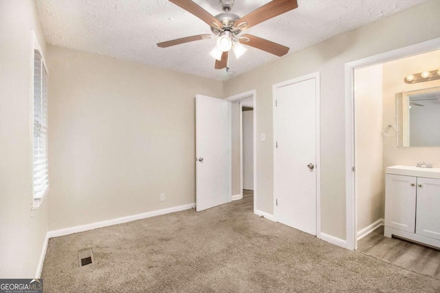 unfurnished bedroom featuring a textured ceiling, light carpet, ceiling fan, and ensuite bathroom