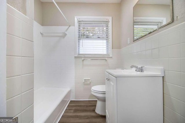 full bathroom featuring toilet,  shower combination, tile walls, hardwood / wood-style floors, and vanity