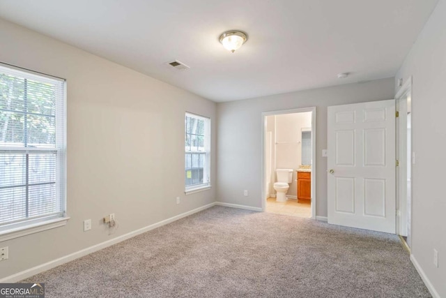 unfurnished bedroom with ensuite bathroom, light colored carpet, and multiple windows