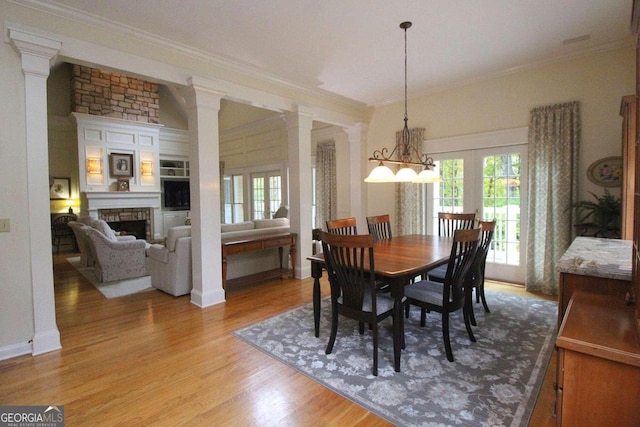 dining space featuring french doors, a fireplace, crown molding, light wood-type flooring, and a chandelier