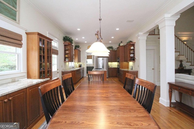 dining room with decorative columns, light wood-type flooring, sink, and crown molding