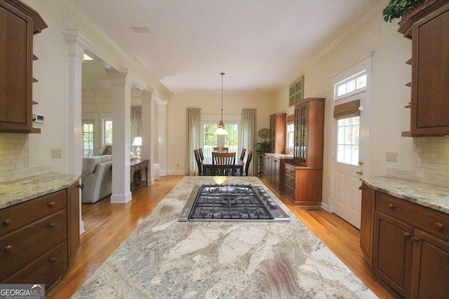 kitchen featuring light stone counters, crown molding, backsplash, light hardwood / wood-style floors, and decorative columns