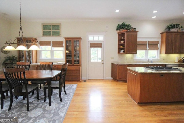 kitchen featuring decorative light fixtures, light stone countertops, decorative backsplash, stainless steel gas stovetop, and light hardwood / wood-style flooring