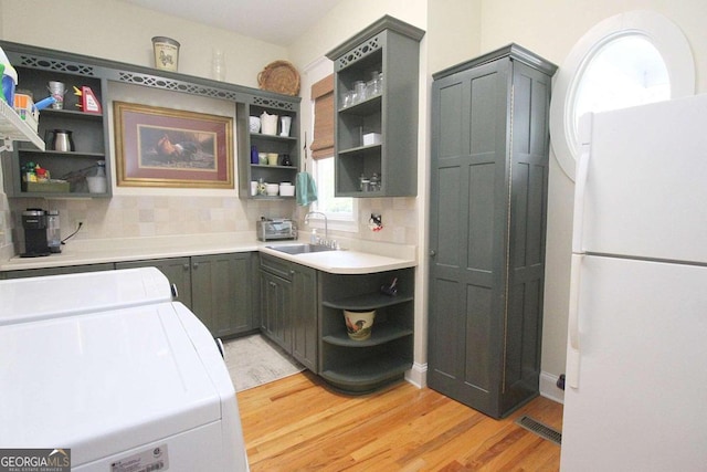 kitchen featuring separate washer and dryer, sink, light hardwood / wood-style flooring, white fridge, and decorative backsplash