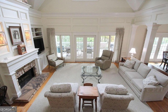 living room with high vaulted ceiling, hardwood / wood-style floors, a stone fireplace, and french doors