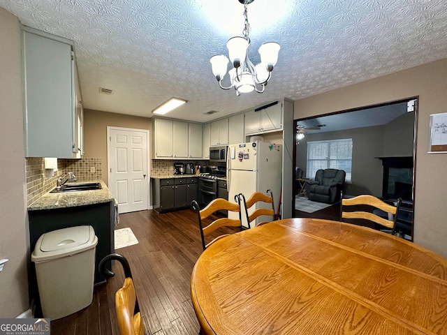 dining area featuring sink, ceiling fan with notable chandelier, a textured ceiling, a fireplace, and dark hardwood / wood-style flooring