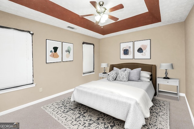 carpeted bedroom with ceiling fan and a tray ceiling