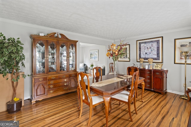 dining space featuring wood-type flooring, ornamental molding, and a textured ceiling