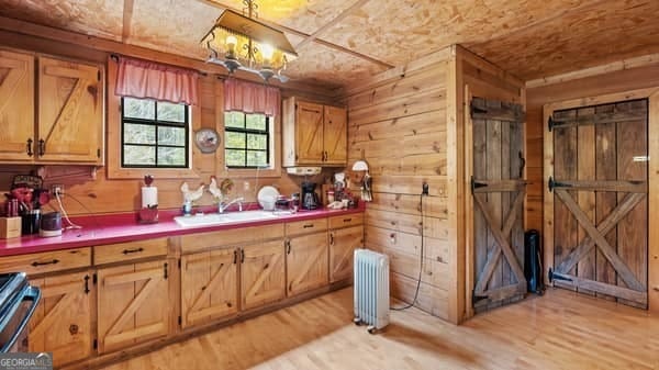 kitchen with stainless steel range, sink, radiator heating unit, light hardwood / wood-style flooring, and wood walls