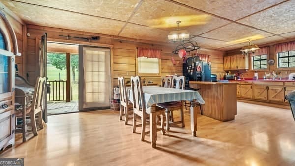 dining area featuring light hardwood / wood-style floors, a notable chandelier, a healthy amount of sunlight, and wood walls