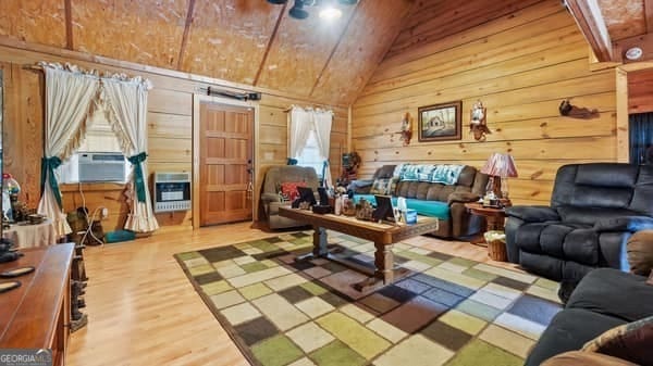 living room featuring hardwood / wood-style floors, cooling unit, wooden walls, vaulted ceiling, and heating unit