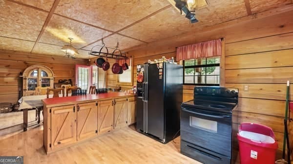 kitchen with a wealth of natural light, wooden walls, light hardwood / wood-style flooring, and black appliances